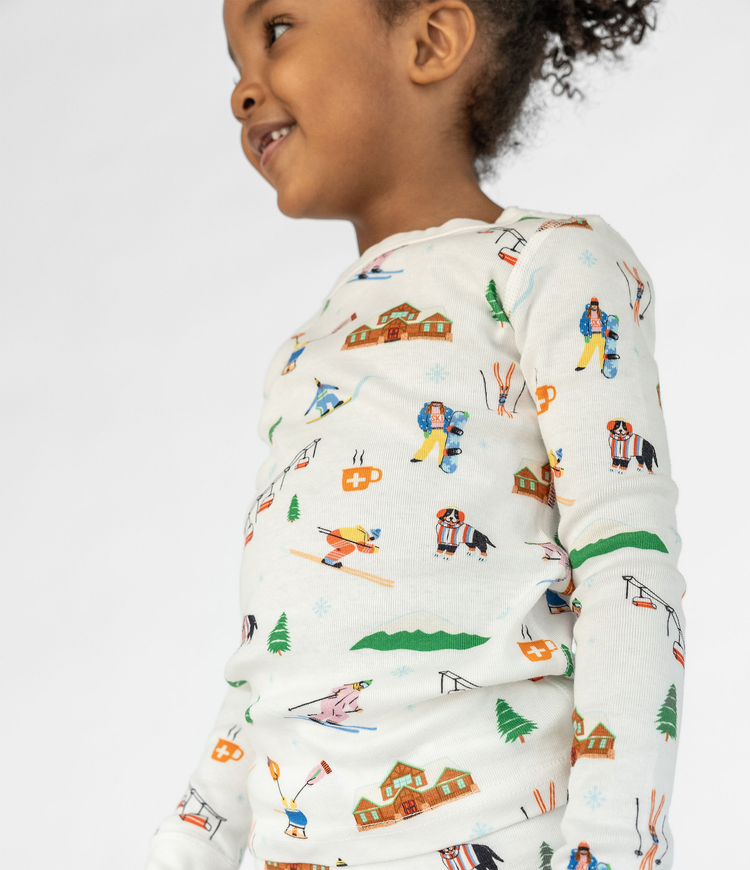 Child Wearing Smaller Things Pajama Set - Colorful Ski Resort Print Featuring Skis, Snowboards, Dogs, and Cabins on 100% Organic Cotton