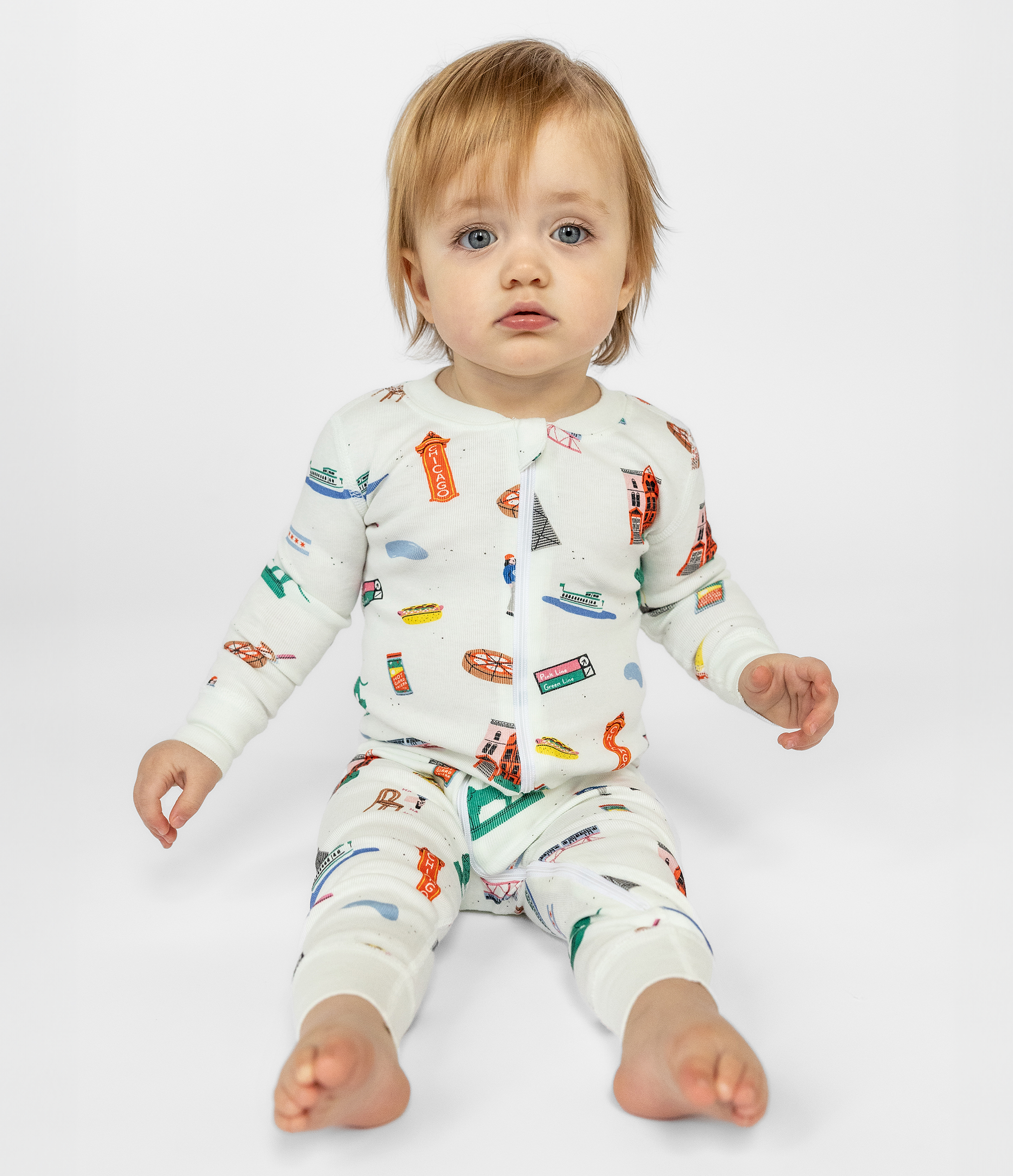 Blue Eyed Toddler Wearing White Fun Chicago Themed Sleepwear. 100% Organic Cotton. Zip-up Long Sleeve Comfortable and Cozy Pajamas for Babies and Toddlers.