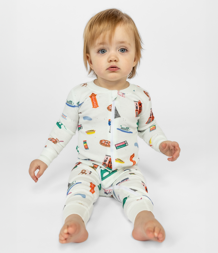 Blue Eyed Toddler Wearing White Fun Chicago Themed Sleepwear. 100% Organic Cotton. Zip-up Long Sleeve Comfortable and Cozy Pajamas for Babies and Toddlers.
